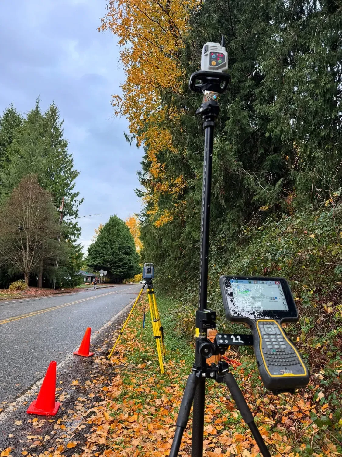 Total station and data collector set up along a roadway shoulder with traffic cones during a record survey.